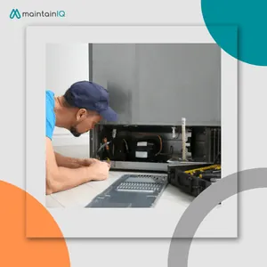 Technician kneeling to reach the condenser coil behind the vent at the bottom of a refrigerator